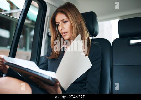 Getting work done on the go. a mature businesswoman going through paperwork in the back seat of a car. Stock Photo