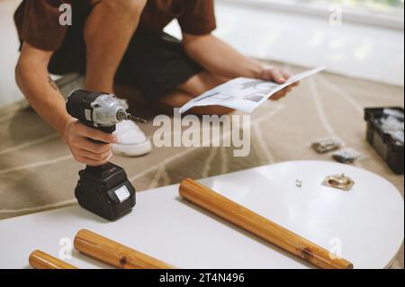 Young man using power drill when when assembling coffee table Stock Photo