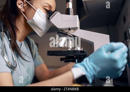 Asian doctor with medical mask and gloves looks into microscope at table in laboratory Stock Photo