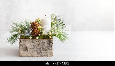 Christmas composition of candle, pine cones, fir branches, flowers and winter berries in wooden box. Cozy home winter concept. Stock Photo