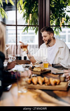 Happy young man drinking draft beer while having fun in pub or bar with friends and laughing Stock Photo