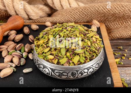 Chopped cut pistachio nuts Concept. Pistachios prepared for presentation in a copper bowl and on black marble. Ground, Milled, Crushed or Granulated P Stock Photo