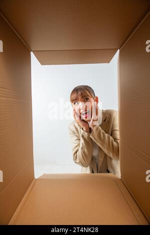 young woman feels overjoyed getting long-awaited parcel with goods smile, view from bottom of box. Stock Photo