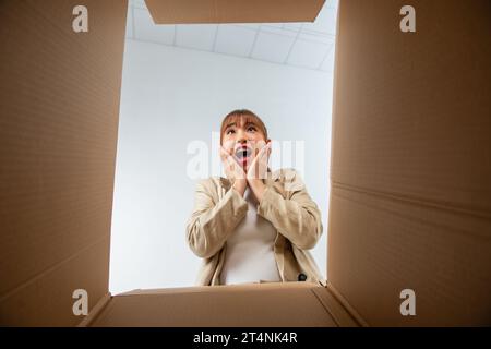 A young woman opens up a box, surprised and happy to see their order better than expected Stock Photo