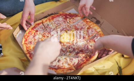 Young students' hands reach for the pizza. Stock Photo