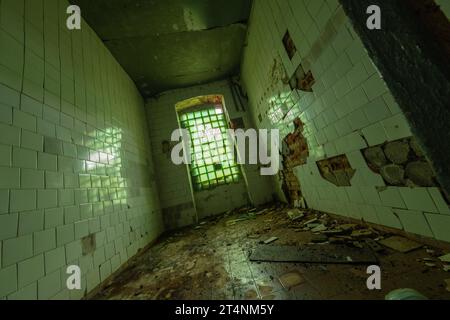 From above view of narrow room with shabby walls broken ceramic tiles, and glass window with fence rubbish trash on uncleaned floor  Stock Photo
