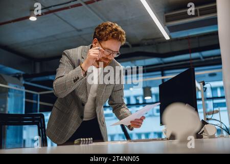 Focused entrepreneur working with documents standing near desk in modern office Stock Photo