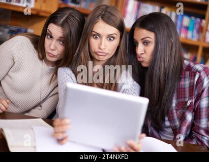 Taking a duck face break. three friends sitting in the library taking photos of themselves with a digital tablet. Stock Photo