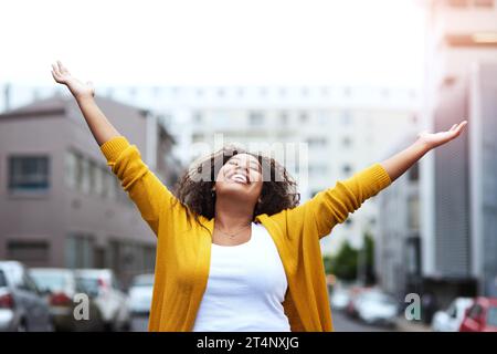 Free like a bird. a happy young woman celebrating with arms raised against a city background. Stock Photo