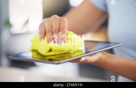 An unrecognizable woman cleaning her digital tablet in her apartment. One unknown woman using a rag to remove dust from her device Stock Photo