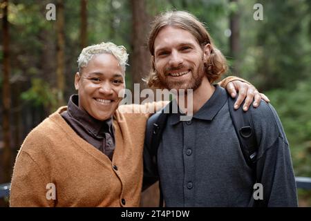 Portrait of multiethnic happy couple embracing and smiling at camera while walking in the forest Stock Photo