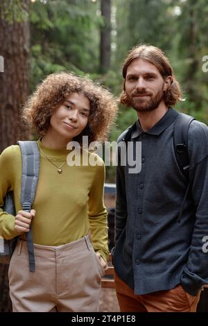 Vertical portrait of young couple looking at camera while hiking in the forest Stock Photo