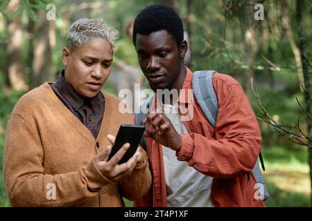 Multiethnic couple watching online map on smartphone during their hiking in the forest Stock Photo