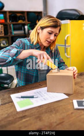 Blonde woman with cutter unpacking order received by courier with merchandise to sell on line Stock Photo