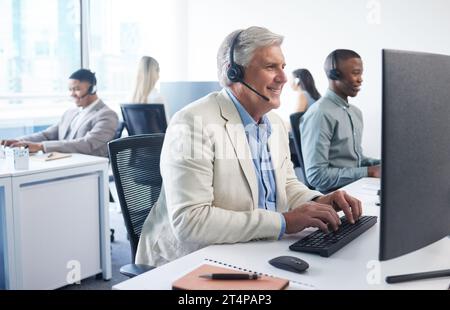 We have an amazing offer for you. a mature businessman using a headset and computer in a modern office. Stock Photo