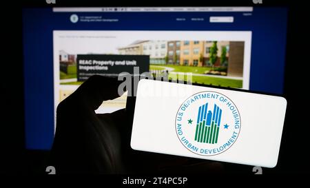 Person holding cellphone with logo of American Department of Housing and Urban Development (HUD) in front of webpage. Focus on phone display. Stock Photo