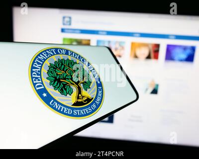 Cellphone with seal of United States Department of Education in front of website. Focus on center-left of phone display. Stock Photo