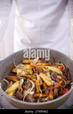 Hands holding casserole with a typical Peruvian dish called Lomo saltado. Stock Photo