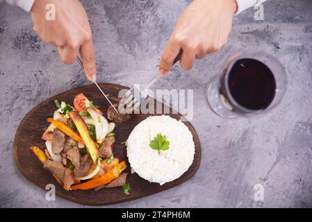 Hands picking up a piece of meat with a fork and knife, from a typical Peruvian dish called Lomo saltado, seen from above. Stock Photo