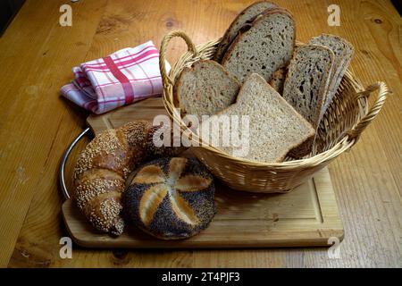 Basket with different types of bread, sesame croissant and poppy seed rolls on a wooden board Stock Photo