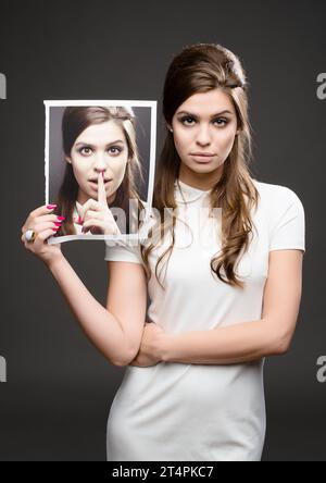 There are two sides to every story. Studio shot of an attractive young woman dressed up in 60’s wear and holding a photograph of herself whispering Stock Photo