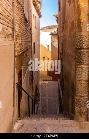 Stone staircase on a narrow medieval cobbled street with old residential houses with tiled roofs, neglected facades and street lamps, Toledo, Spain Stock Photo