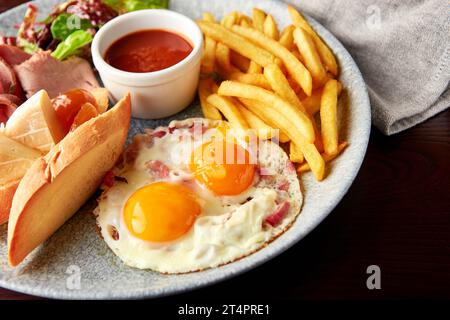 Full English Breakfast including ham, egg with bacon, french fries, lettuce salad, cheese and bread with tomato sauce. Stock Photo