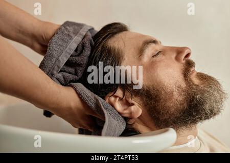 Young bearded man washing his hair in barber shop before haircut Stock Photo