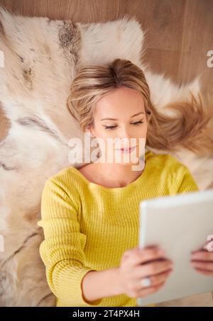 She looks good fom every angle. A young woman lying on the ground holding a digtal tablet. Stock Photo