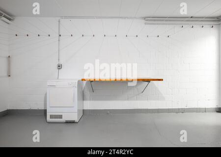 Apartment building common use empty laundry room. Empty wooden table top, dryer and hanging wires on the wall. Wide-angle view, no people. Stock Photo