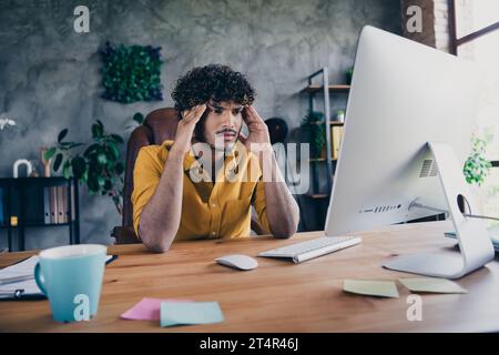 Photo portrait of attractive man wear yellow shirt touch temples confused depressed overworked table modern workplace room home design Stock Photo