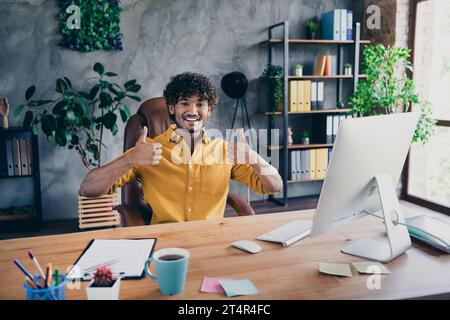 Photo of positive funny man it specialist hacker demonstrate thumbs up nice feedback workspace indoors Stock Photo