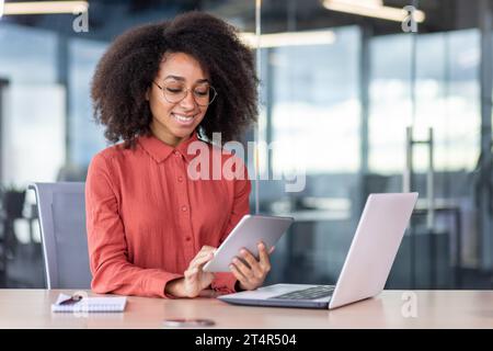 Young successful businesswoman at workplace is satisfied with results of achievement at work smiling and using tablet computer, programmer is testing new software in application Stock Photo