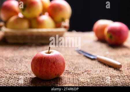 Ripe apples on burlap and in a basket on a black background. Rustic style, close-up. Stock Photo
