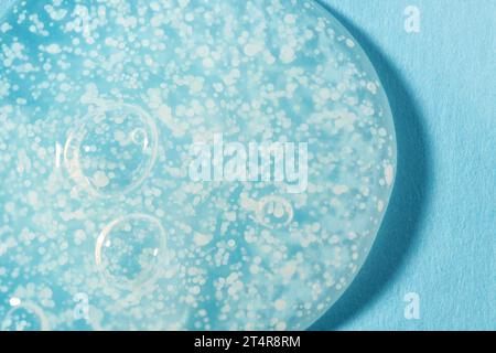 Smoothing scrub wash gel drop on blue background. Clear liquid gel with polishing beads for gentle exfoliation swatch closeup. Stock Photo