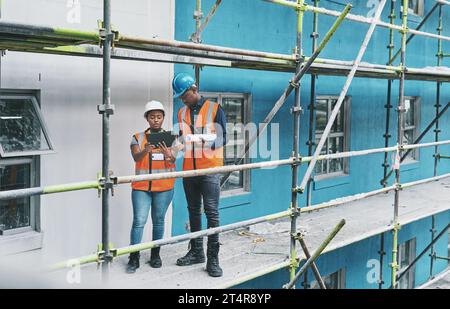 Adopting technology to ramp up the development on a new site. a young man and woman using a digital tablet while working at a construction site. Stock Photo
