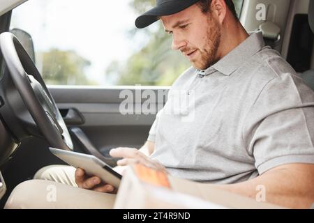 Whats the address again. a handsome young delivery man using a tablet while sitting in his van. Stock Photo