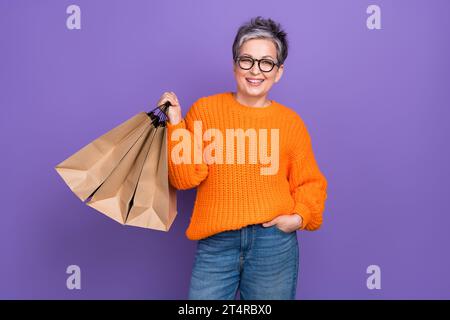 Photo of senior business lady wearing orange knitted sweater hold packages paper bargains shopping isolated on violet color background Stock Photo