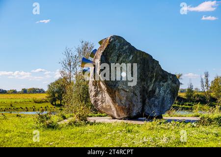 Huge stone with metal speakers as decoration in the fishing pond with the plain Dutch meadow against the blue sky in the background, sunny day in Meer Stock Photo