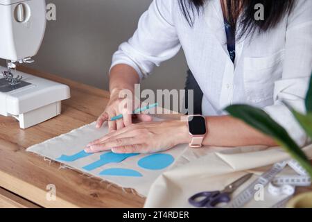 Young adult woman working on sewing patterns for handmade doll, drawing on cloth. Creative hobby and lifestyle concept. Stock Photo