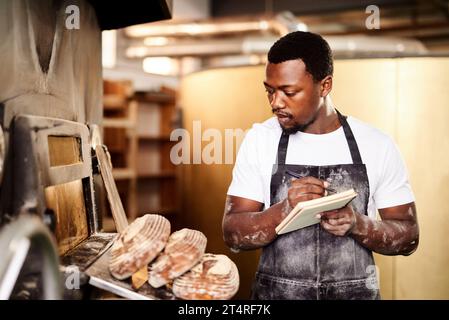 Lets count how many I just removed from the oven. a male baker making notes while working in his bakery. Stock Photo