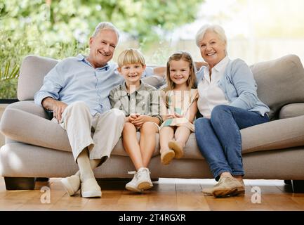 Portrait of an affectionate family of four sitting comfortable on their sofa in the living room at home. A grandmother, grandfather, grandson and Stock Photo