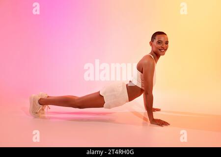 Positive young latin lady in sportswear does push-ups, plank workout on floor Stock Photo