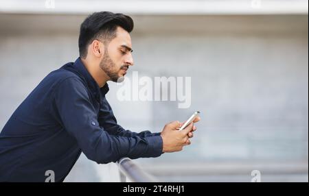 Concerned Arabic businessman scrolling through smartphone amidst urban city background Stock Photo