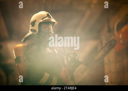 Firefighter portrait wearing full equipment, oxygen mask and chain saw. Smoke and fire trucks in the background. Stock Photo