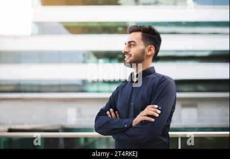 Confident arabic young guy posing against modern business building Stock Photo
