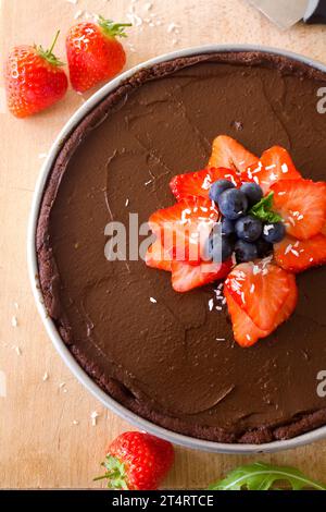 Double chocolate tart shot from above decorated with fresh strawberries, blueberries and coconut on a wooden background. Stock Photo