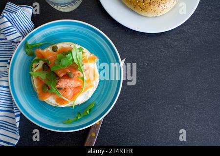 Smoked salmon bagel with cream cheese, capers and arugula shot from above on a grey slate background. Stock Photo