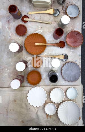 Handmade ceramic scallop plates and bowls being glazed in various coloured glazes Stock Photo
