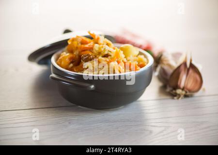 Cooked classic pilaf with meat, raisins, garlic and other ingredients in a bowl on a wooden table. Stock Photo